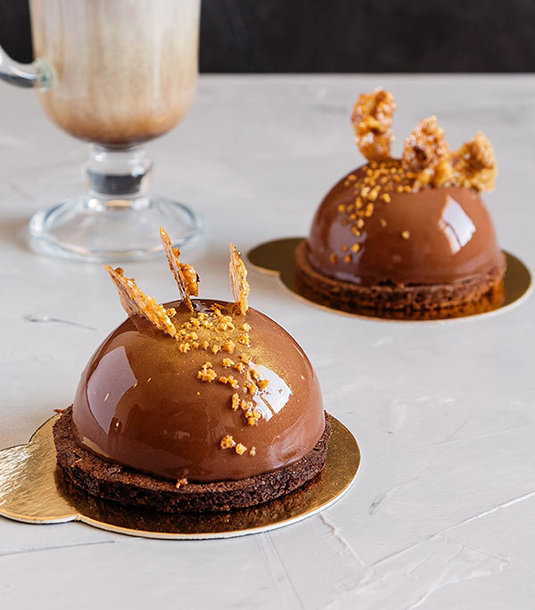 Two chocolate cakes with a glass of coffee in the background.