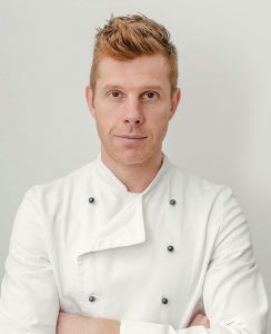 A man in white chef 's jacket posing for the camera.