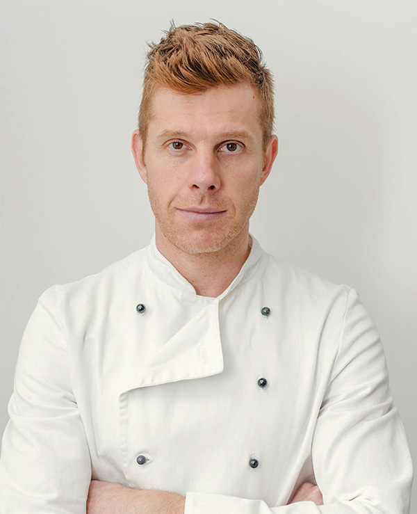 A man in white chef 's jacket posing for the camera.