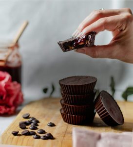 A person holding a chocolate bar over some peanut butter cups.