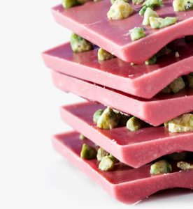A stack of pink chocolate with nuts on top.