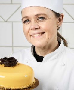 A woman in chef 's outfit holding a cake.