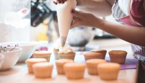 A person decorating cupcakes with frosting on top of a table.