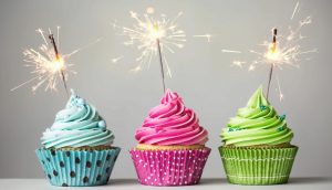Three cupcakes with a sparkler in the background.