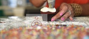 A person is decorating a cupcake with white frosting.