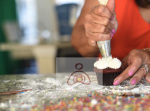 A person decorating cupcakes with frosting on top of a table.