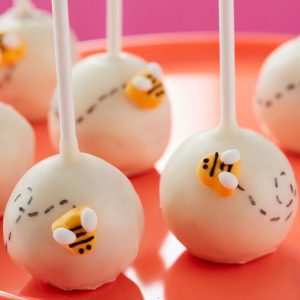 A plate of cake pops with bees on them.
