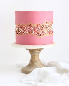 A pink cake with gold and silver decorations on top of it.