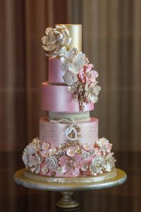 A pink and gold wedding cake with flowers