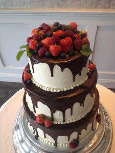 A three layer cake with chocolate and berries on top.