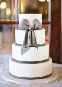 A white cake with grey ribbon on top of it.