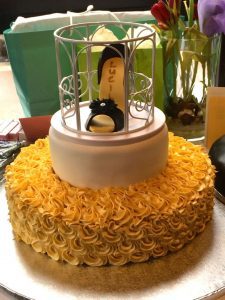 A cake with yellow frosting and a penguin on top.