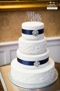 A white wedding cake with blue ribbon and silver monogram.