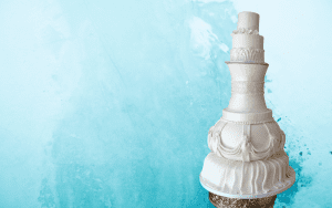 A white wedding cake is sitting on top of a gold stand.