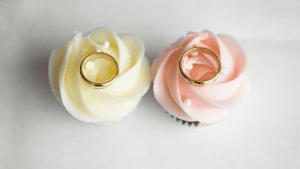 Two cupcakes with a gold wedding ring on top of them.
