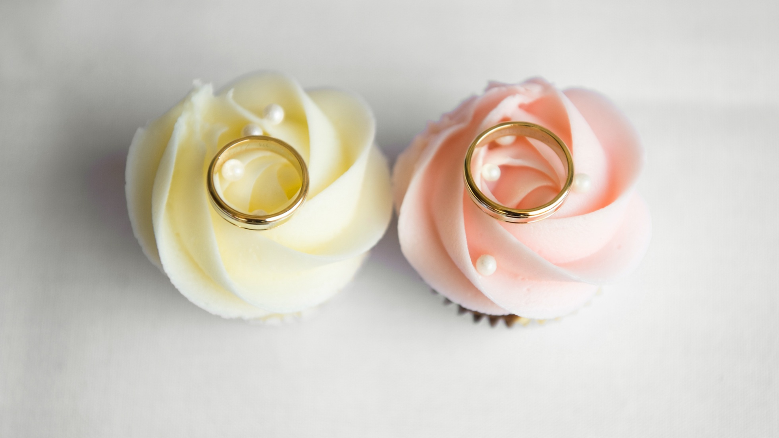 Two cupcakes with a gold wedding ring on top of them.