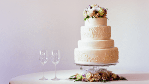 A wedding cake and two wine glasses on the table.