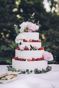A three layer cake with strawberries and flowers on top.