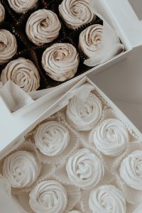 A box of cupcakes with white frosting in the shape of roses.